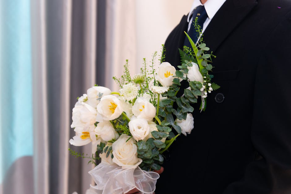A bouquet arranged with deep red roses, soft pink roses, and white blossoms, complemented by small clusters of white filler flowers and lush green foliage. The bouquet is wrapped with cream-colored ri